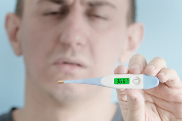 Electronic thermometer in a man's hand. Man feigning illness in the background.