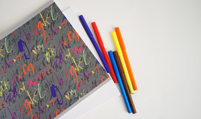 different felt-tip pens near a sketchbook on a white background