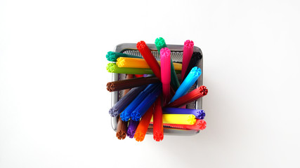 multi-colored felt-tip pens stand in a mesh transparent glass on the isolated background