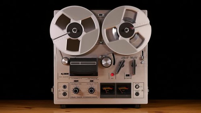 Vintage Reel to Reel tape recorder playing music isolated on black background