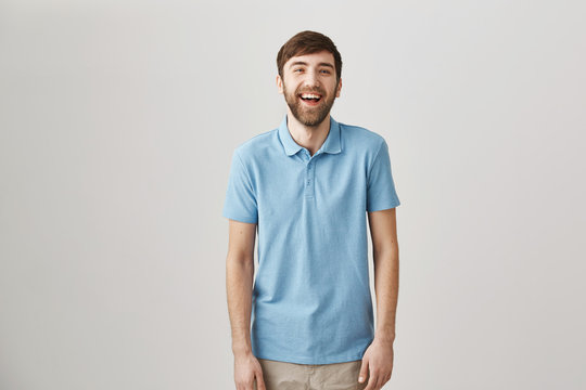 Sense of humour makes man unique. Portrait of slender ordinary caucasian guy with beard and moustache laughing and smiling while standing over gray background, watching comedy with girlfriend