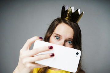 cute blue-eyed girl with a crown on her head makes selfie on her smartphone