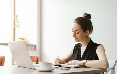 Beautiful girl working out a plan of the project and concept. Girl paints a website design on a laptop. student prints a message on the phone in the messenger. Development. Digital marketing