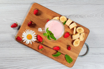 Glass of milk shake with mint and fresh strawberries, banana on a wood cutting board