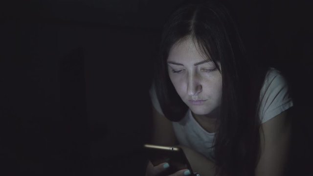 Young woman in the dark at night sits with a phone in social networks.