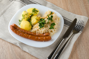Roasted sausages with steamed cabbage (sauerkraut) and boiled potatoes in white plate.