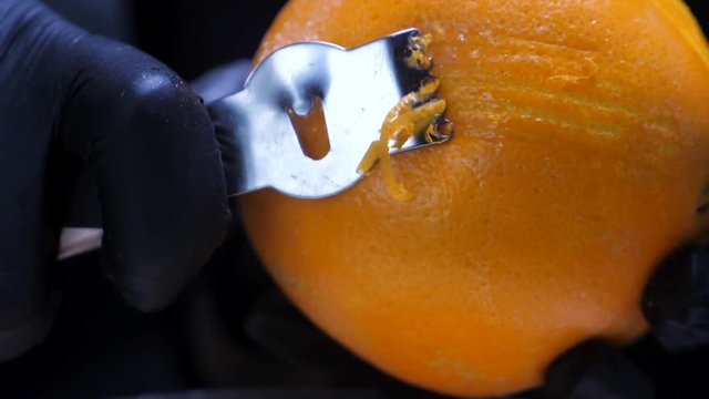 Slow motion of citrus zester grating peeling orange peel, oils spraying against dark background