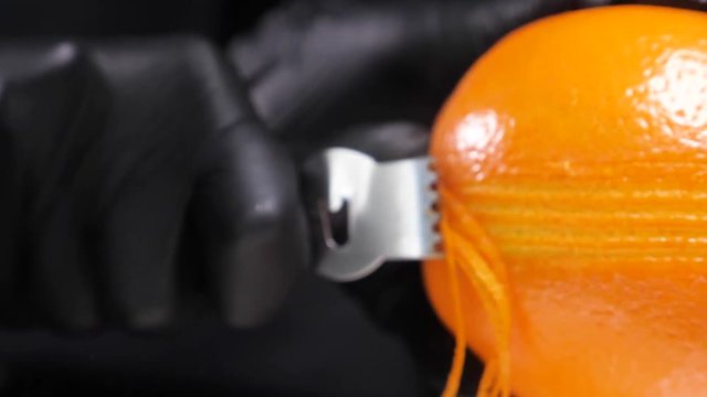 Slow motion of citrus zester grating peeling orange peel, oils spraying against dark background