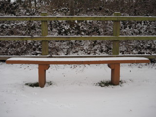 Empty wooden bench seat perfectly covered with white snow in the winter