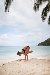 Beautiful young woman is doing yoga near the sea and drinks coconut