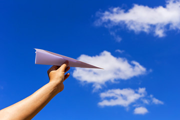 Holding paper airplane before throwing with blue sky background.