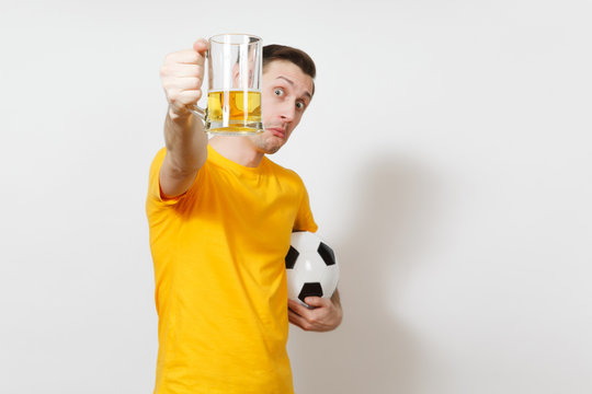 Inspired young fun European man, fan or player in yellow uniform hold in front face pint mug of beer, soccer ball cheer favorite football team isolated on white background. Sport, lifestyle concept.
