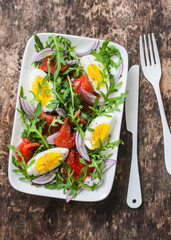 Smoked salmon, eggs, arugula, red onion, olive oil, lemon dressing salad on wooden background, top view