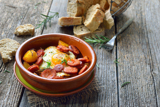 Spanisches Tapa: Gebratene scharfe Chorizo Bratwurst mit Spiegelei und kleinen Kartoffeln &ndash; Spanish tapa: Spicy chorizo sausage with fried egg and baby potatoes served in a terra cotta cazuela dish