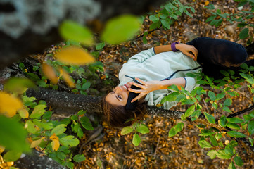 Young woman lying on a branch, in a tree, talking on her smart phone, smiling and feeling relaxed in nature in autumn season