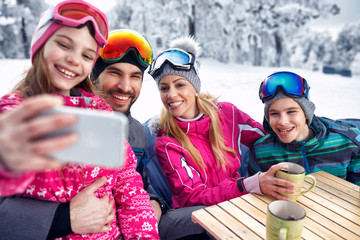 family laughing and enjoying in winter vacation together on snow and making selfie