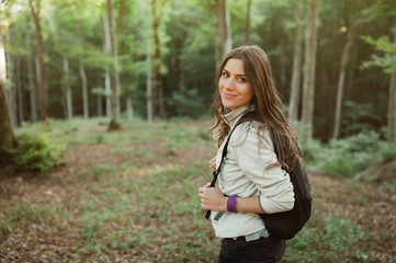 Pretty young woman smiling happy carrying backpack in the forest on sunset light in the autumn season.