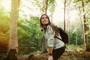 Pretty young woman smiling happy carrying backpack in the forest on sunset light in the autumn season.