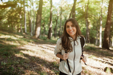 Pretty young woman smiling happy carrying backpack in the forest on sunset light in the autumn...