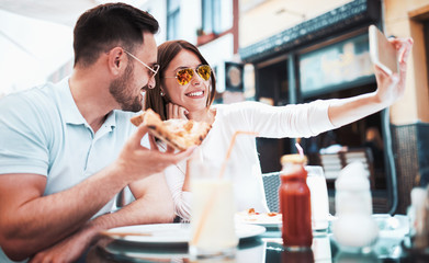 Beautiful young couple sitting in the cafe and eating pizza. Consumerism, food, lifestyle concept