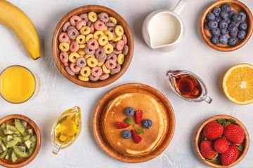 Breakfast with colorful cereal rings, pancakes, fruit, milk, juice.