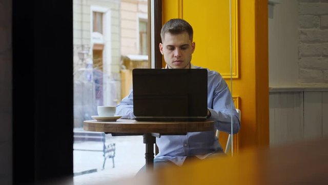 Young businessman using notebook and drinking coffee in cafe.