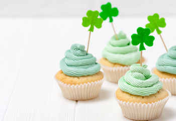 St. Patrick's Day theme colorful horizontal banner. Cupcakes decorated with green buttercream and craft felt decorations in form of shamrock leaves on white background. Copy space. For greeting card