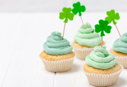 St. Patrick's Day theme colorful horizontal banner. Cupcakes decorated with green buttercream and craft felt decorations in form of shamrock leaves on white background. Copy space. For greeting card - Powered by Adobe