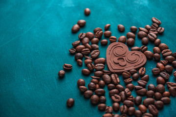heart of dark chocolate lie among coffee beans on a dark background
