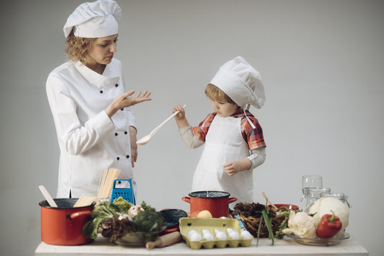 Mother teaches son to cook on light background