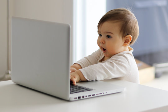 Little baby curiously looking at laptop with open mouth, surprised, child and computer concept