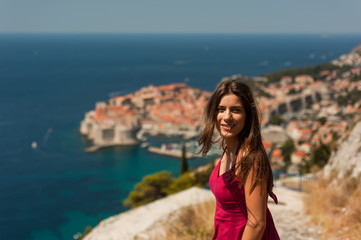 Laughing young woman-traveler having a good time visiting the city of Dubrovnik in Croatia. Picture taken from the mountain above Dubrovnik citadel, Croatia, Famous European Travel Destination.