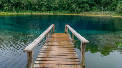 Perspective view of wooden pier in the blue water lake, trees background