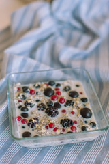 Brekfast bowl of cereal porridge and fruits on tablecloth. Grapes, blueberries, blackberris, raspberris, red currants, black currant. Healthy food concept.