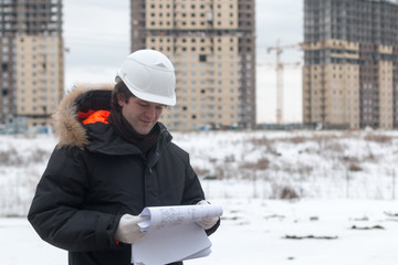 Worker or engineer holding drawing in hands and reading it on background of new apartment buildings and construction cranes on background.Architect engineer concept. Soft focus.