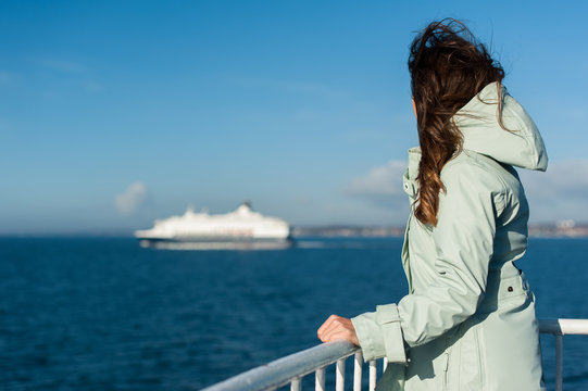 Young traveller woman sailing a ferry, with big boat cruise liner or ferry on the background, wearing a rain jacket.