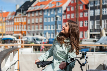 Lovely young woman posing with bike at the Nyhavn harbor pier in european city Copenhagen, Denmark, on sunny day. Visiting Scandinavia, famous European place.
