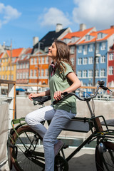 Lovely young woman posing with bike at the Nyhavn harbor pier in european city Copenhagen, Denmark, on sunny day. Visiting Scandinavia, famous European place.