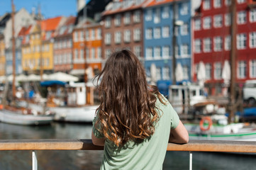 Fototapeta na wymiar Tourist woman admiring the colored old houses, sitting at the Nyhavn harbor pier Copenhagen, Denmark. Visiting Scandinavia, famous European destination.
