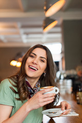 Beautiful girl enjoying a good coffee in the cafe shop, holding a cup and smiling  at camera.