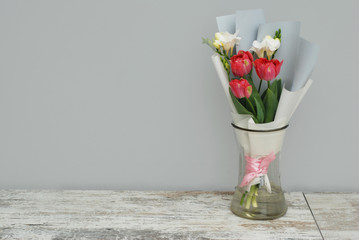 Beautiful bouquet of pink tulips and Freisia Flowers in Glass Vase on gray background. Spring bouquet for Gift with Copy Space.