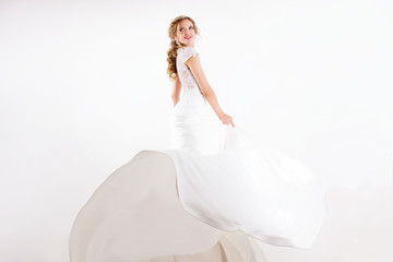 Fototapeta na wymiar young blonde girl in a white wedding dress and jewelry in hairstyle with big curls standing like princess and smiling on a white wall background 