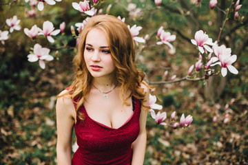 Fototapeta premium Beautiful girl in the flowering cherry blossom. In a burgundy dress with beautiful hair and makeup