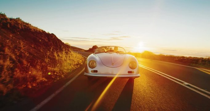 Couple driving into the sunset in classic vintage sports car