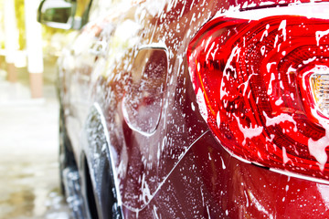 Foam of car wash on red car. Car washing and cleaning background. Closeup tail lamp with copy space.