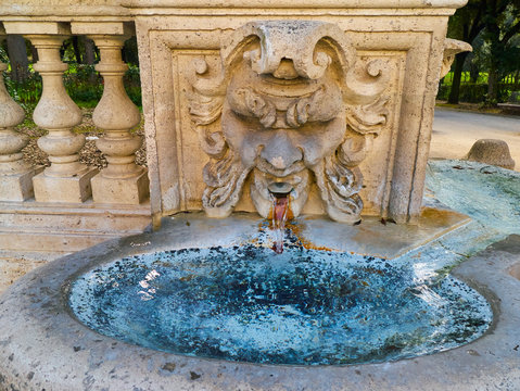 Ancient fountain in form of the anthropomorphic face and bowl with fresh blue water. Park Borghese in Rome, Italy.
