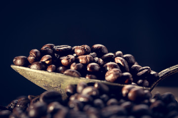 Grains of coffee lie in an old antique spoon. Unusual photo low key.