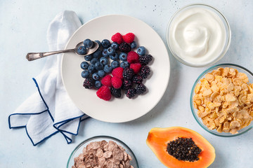 breakfast with berries, yogurt, flakes and cut papaya in a plate on the table. healthy morning
