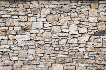 Close-up textured background is an irregular natural stone wall made of different stones without a cement-type bonding mixture. Medieval background