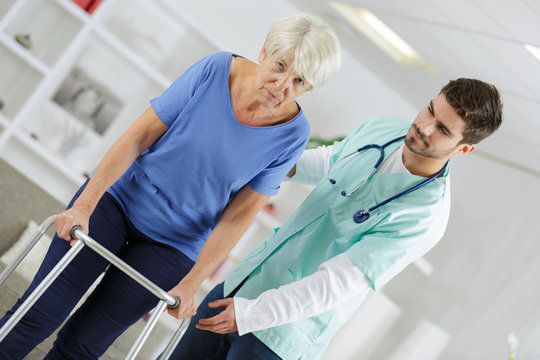 male nurse helping disabled elderly lady with a walking frame